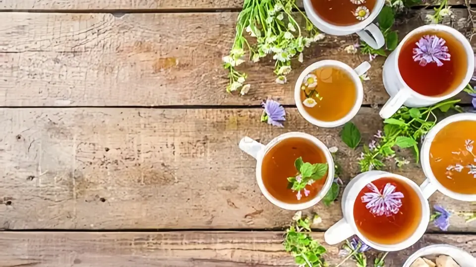 A cup of herbal tea with small bowls of different herbal leaves in the background A cup of herbal tea with small bowls of different herbal leaves in the background