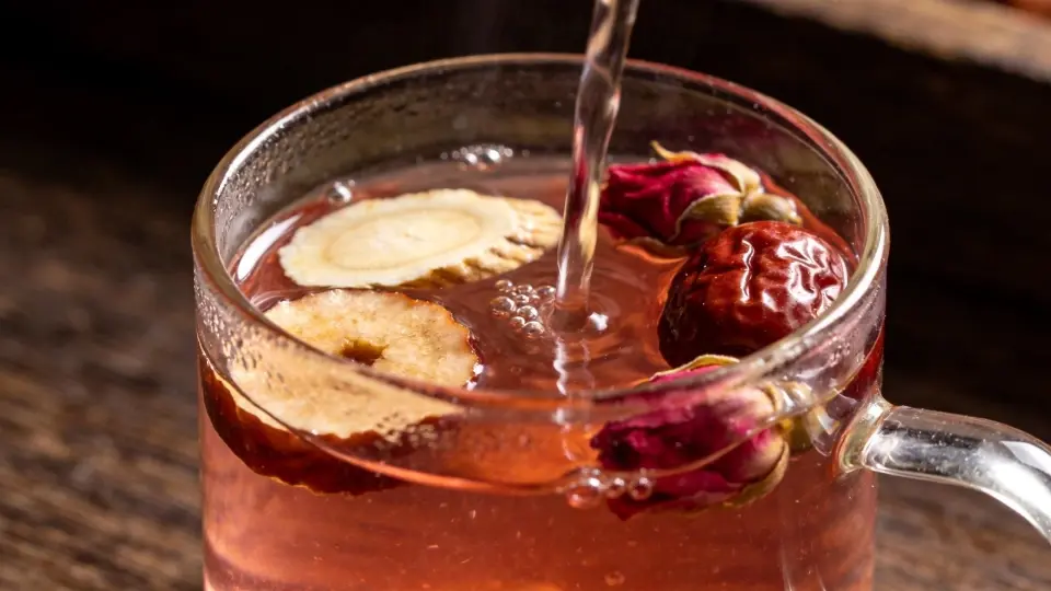 An close-up showcasing natural dried ginger slices, sweet red dates, and dark crimson Pingyin rose buds steeping elegantly in a clean glass teacup